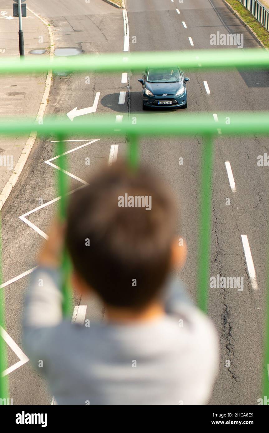 Un jeune garçon regarde les voitures sur une route depuis l'arrière d'une barrière. Banque D'Images