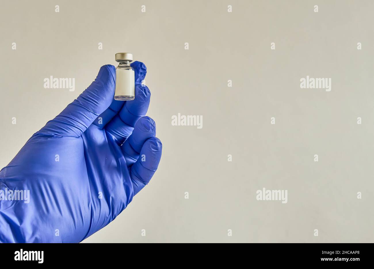 Main avec un gant bleu, tenant un petit flacon contenant un vaccin, sur le point d'être utilisé. Banque D'Images