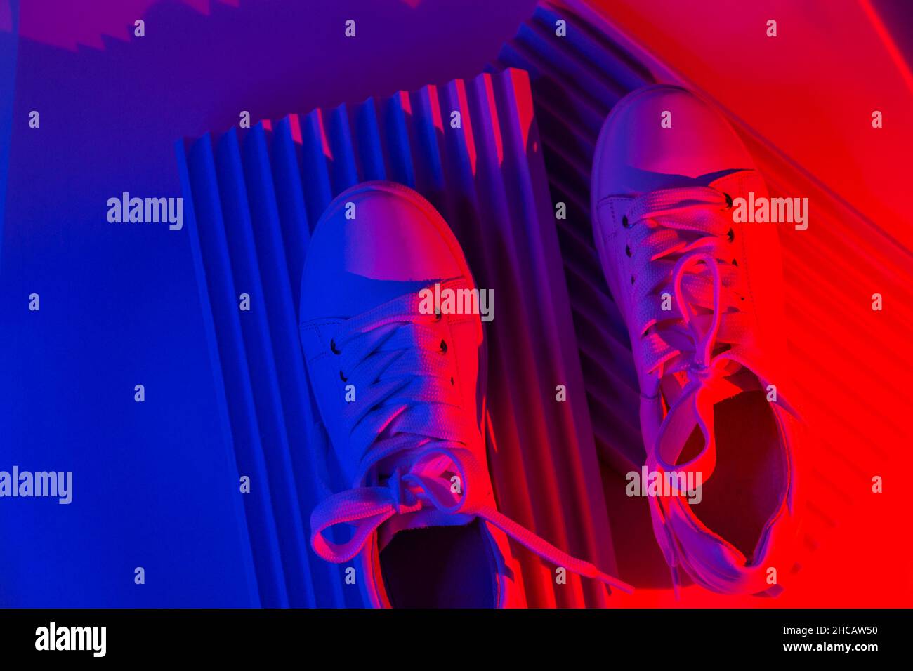 Sneakers tendance blanches sur podium géométrique sur fond abstrait et lumineux.Lumières fluo sur les chaussures décontractées.Lumière à gradient violet et rouge.Minimalisme Banque D'Images