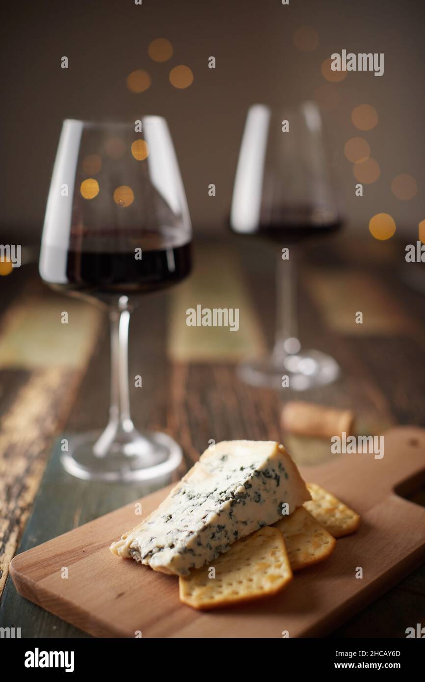 La vie de deux verres de vin, du fromage à la moisissure bleue et des craquelins sur une planche de bois sur le fond d'une guirlande du nouvel an.Vue avant. Banque D'Images