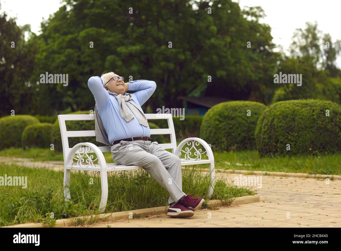 Joyeux smiley homme senior respirant en air frais assis sur un banc dans un parc d'été vert Banque D'Images