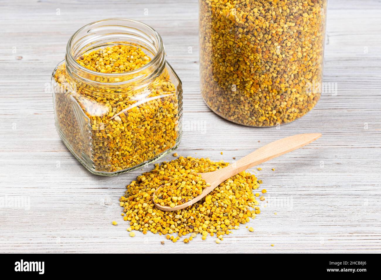 cuillère dans un tas de pollen d'abeille naturel près des pots en verre avec du pain de pollen sur un panneau en bois gris Banque D'Images