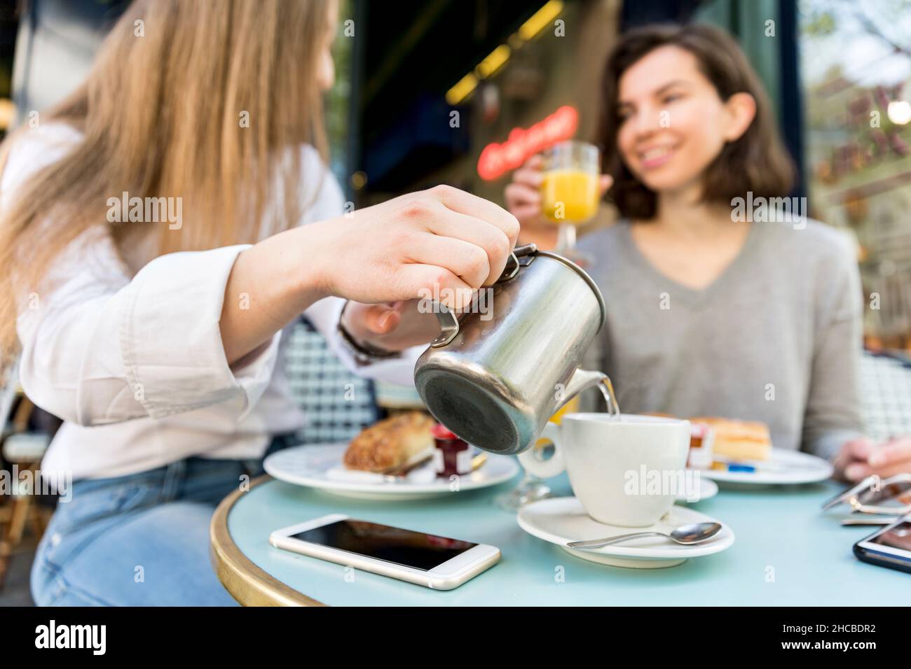 Une jeune femme verse du café dans une tasse pour un ami au café Banque D'Images