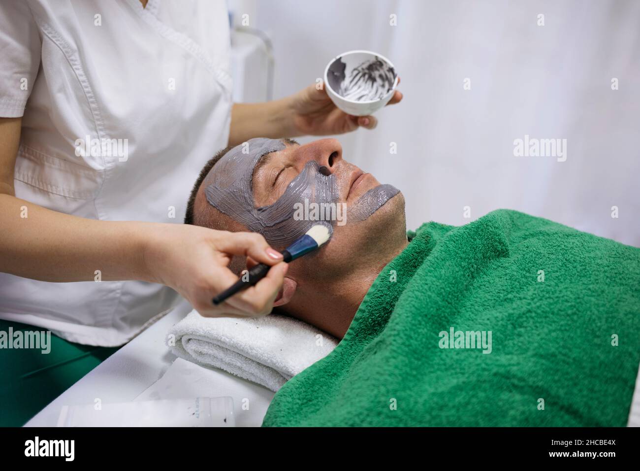 Esthéticienne appliquant le masque facial avec la brosse sur le visage du client dans le salon de beauté Banque D'Images