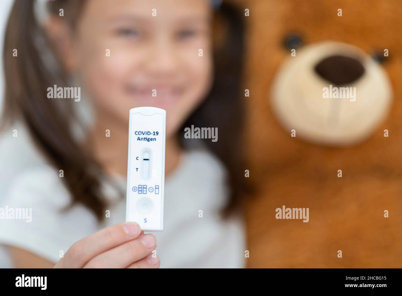 Fille souriante avec ours en peluche montrant un résultat rapide au test de diagnostic Banque D'Images