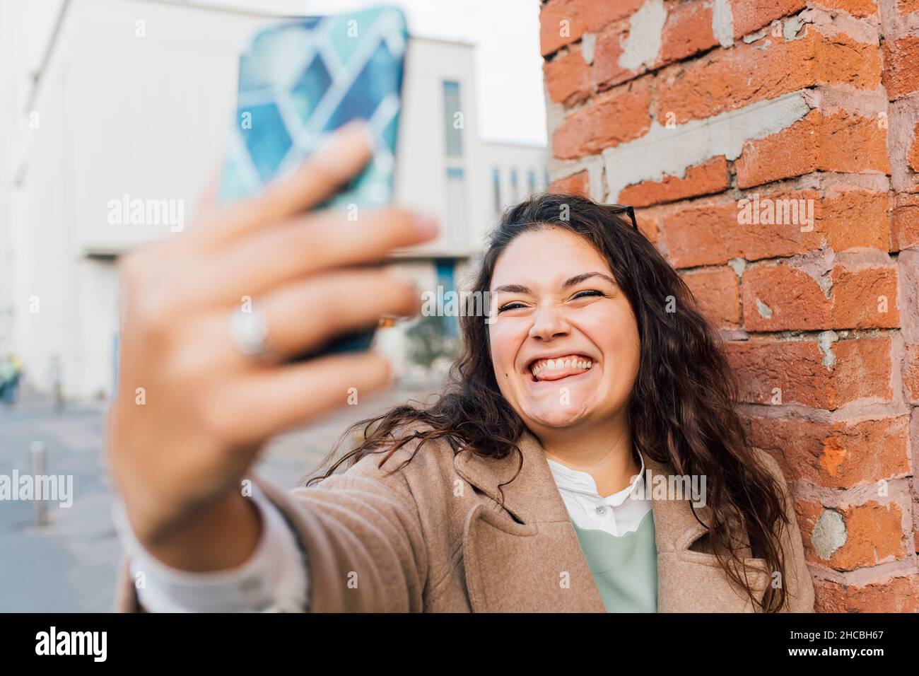 Femme aux courbes qui colle à la langue tout en prenant le selfie sur un téléphone portable Banque D'Images