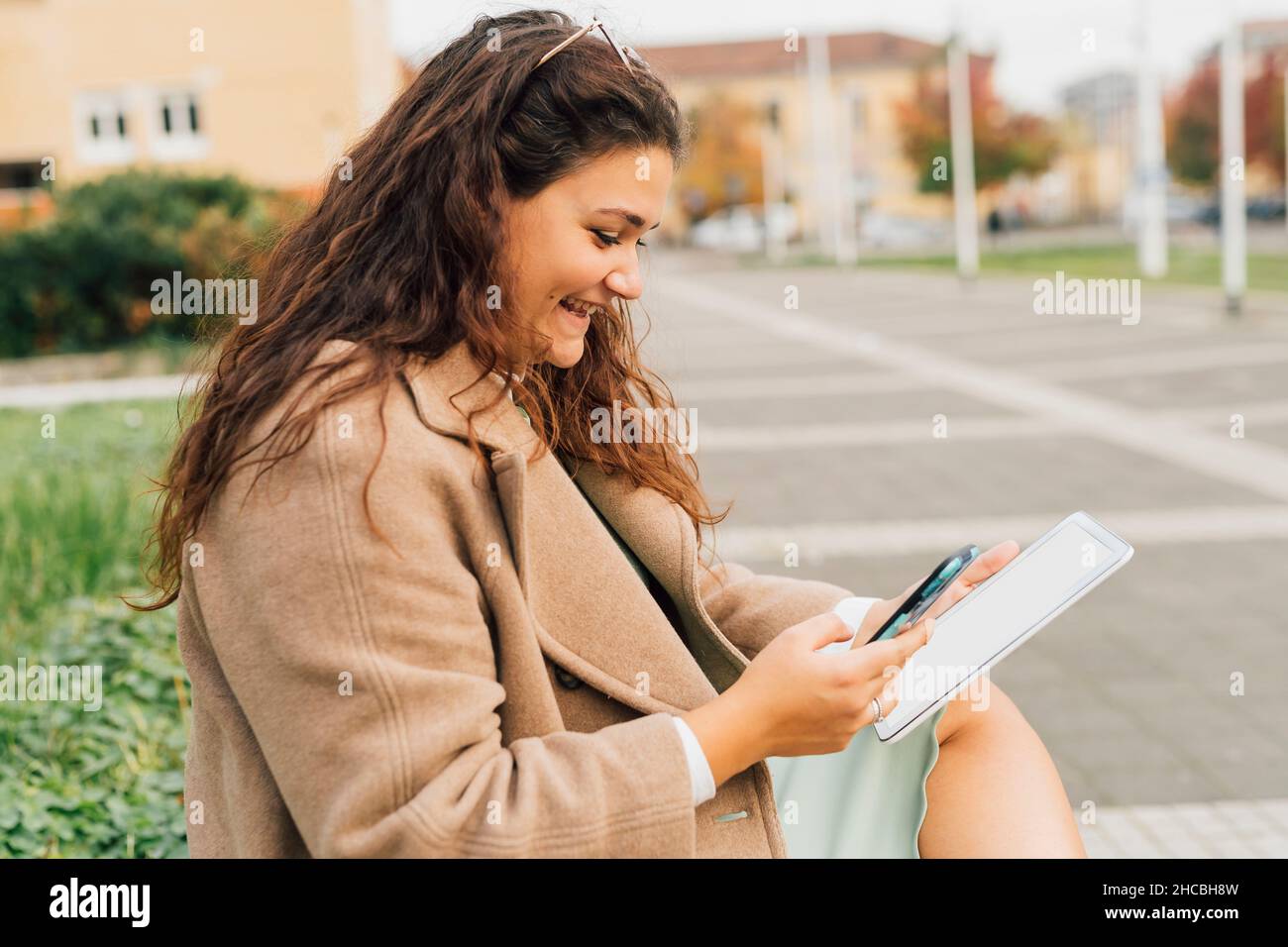 Femme souriante freelance avec une tablette numérique utilisant un smartphone Banque D'Images