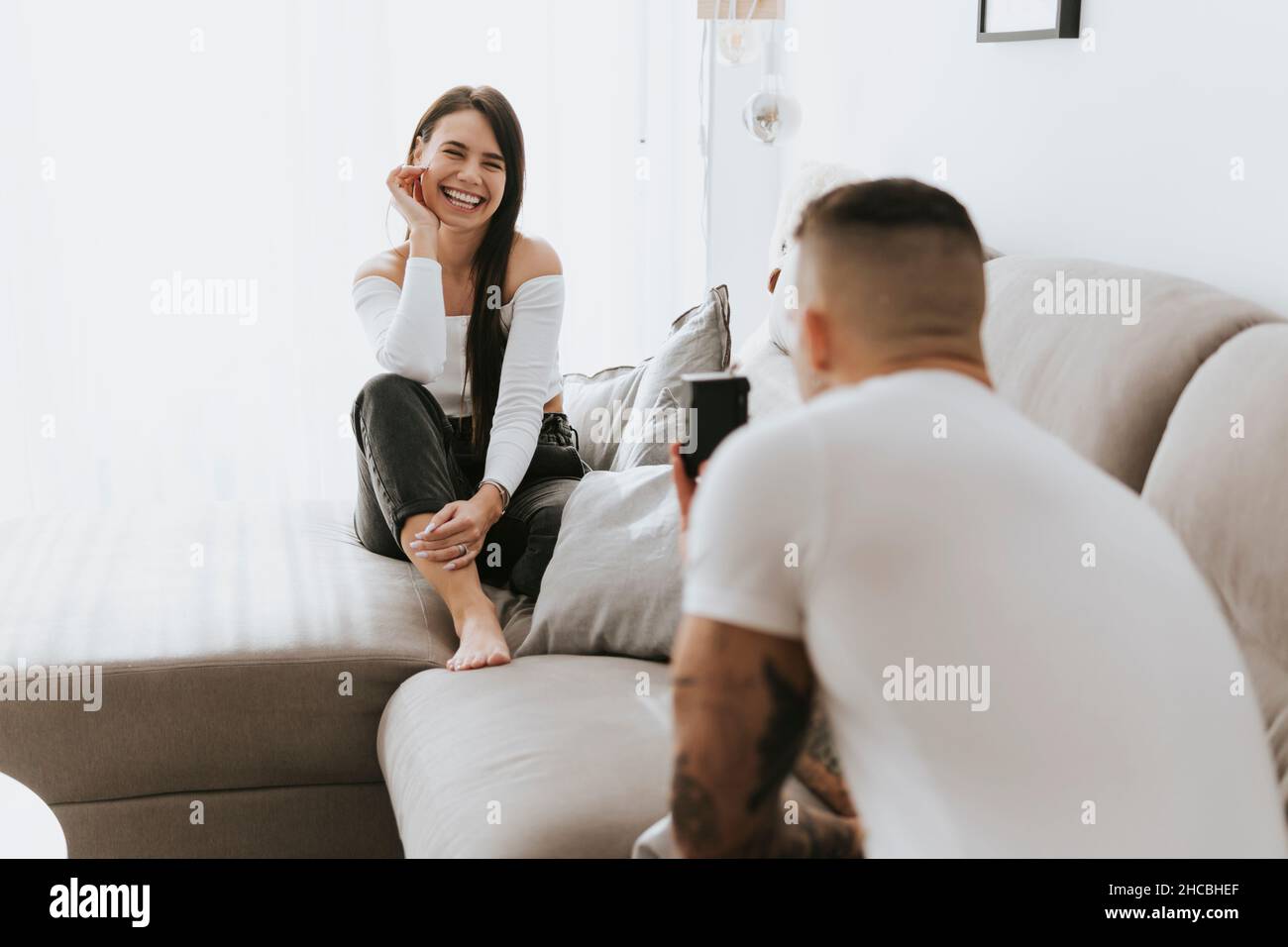 Homme photographiant une femme souriante sur un canapé à travers l'appareil photo Banque D'Images