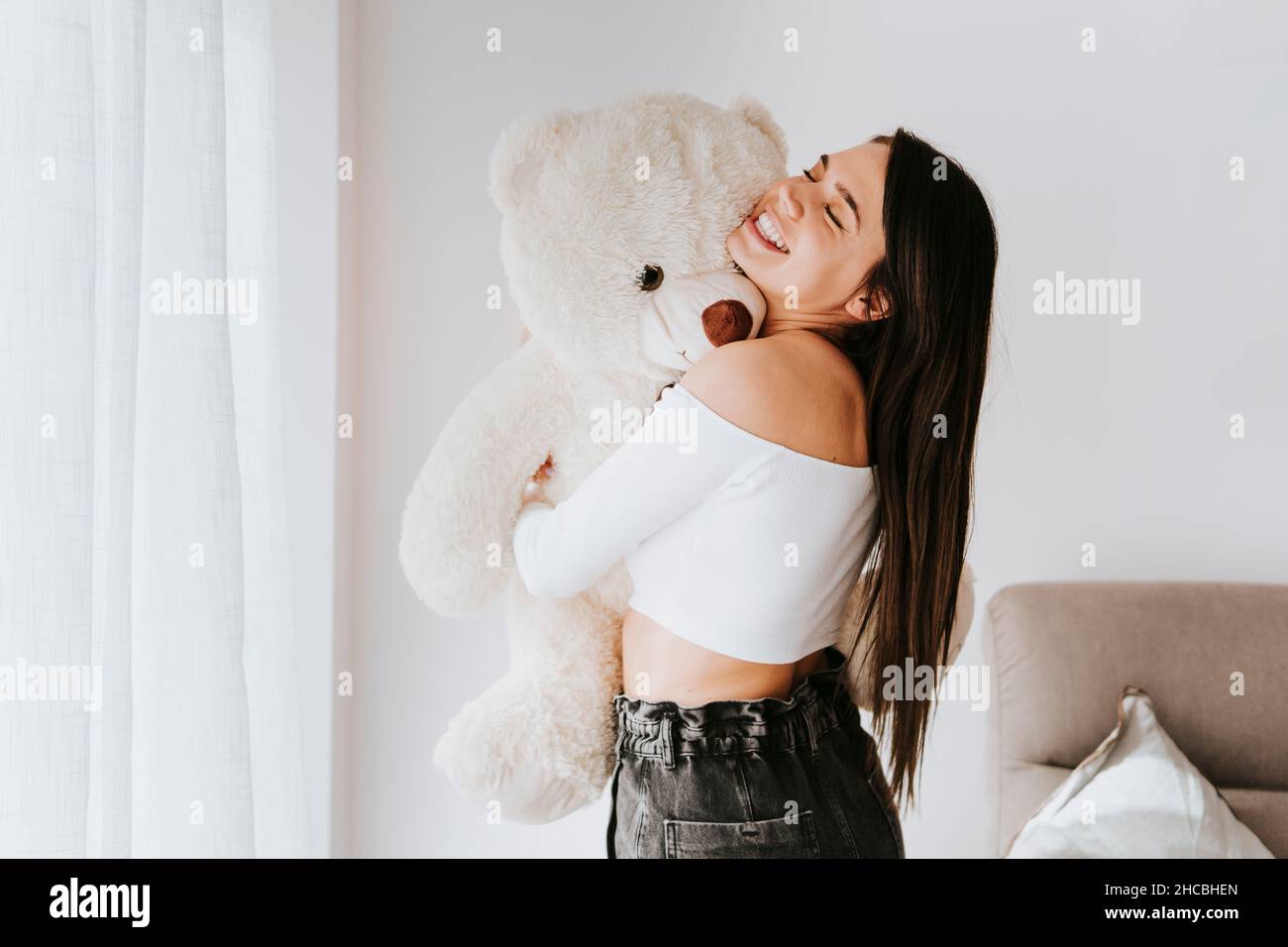 Jeune femme embrassant un ours en peluche à la maison Banque D'Images