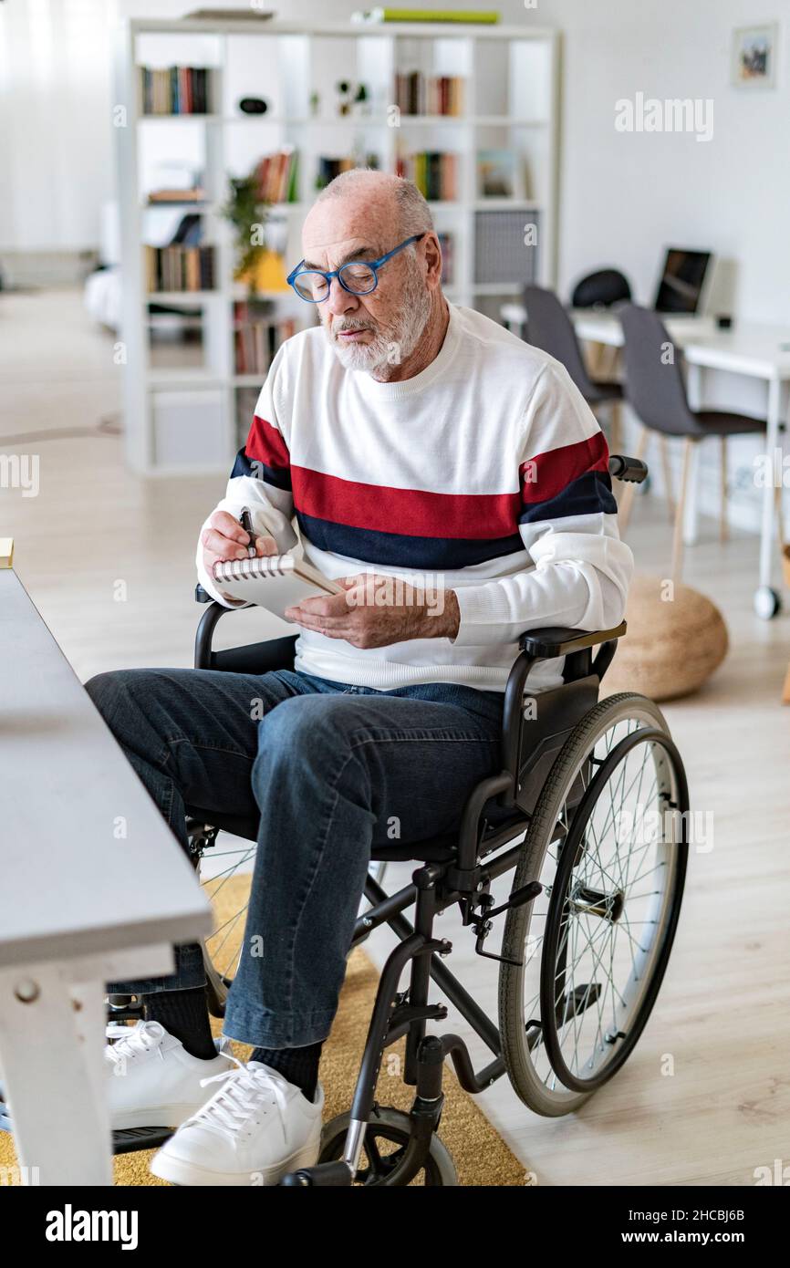 Homme d'affaires senior handicapés écrivant sur le bloc-notes dans la salle de séjour Banque D'Images