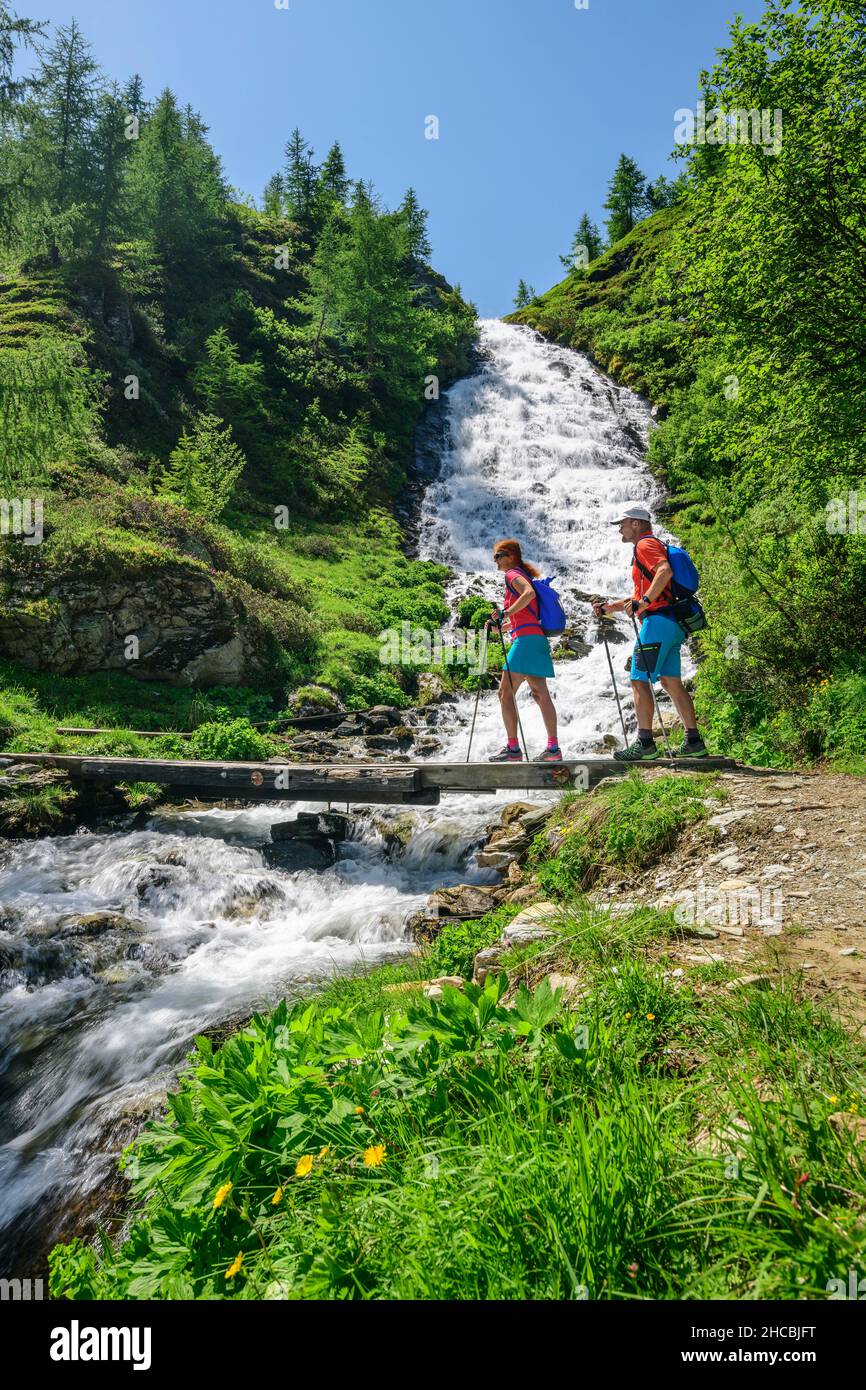 Deux randonneurs traversant le pont au-dessus de la petite cascade dans le parc national Hohe Tauern Banque D'Images