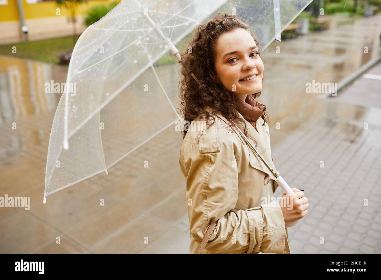 Portrait horizontal haut angle moyen de la belle jeune femme caucasienne portant un trench beige debout à l'extérieur sous un parapluie le jour des pluies smili Banque D'Images