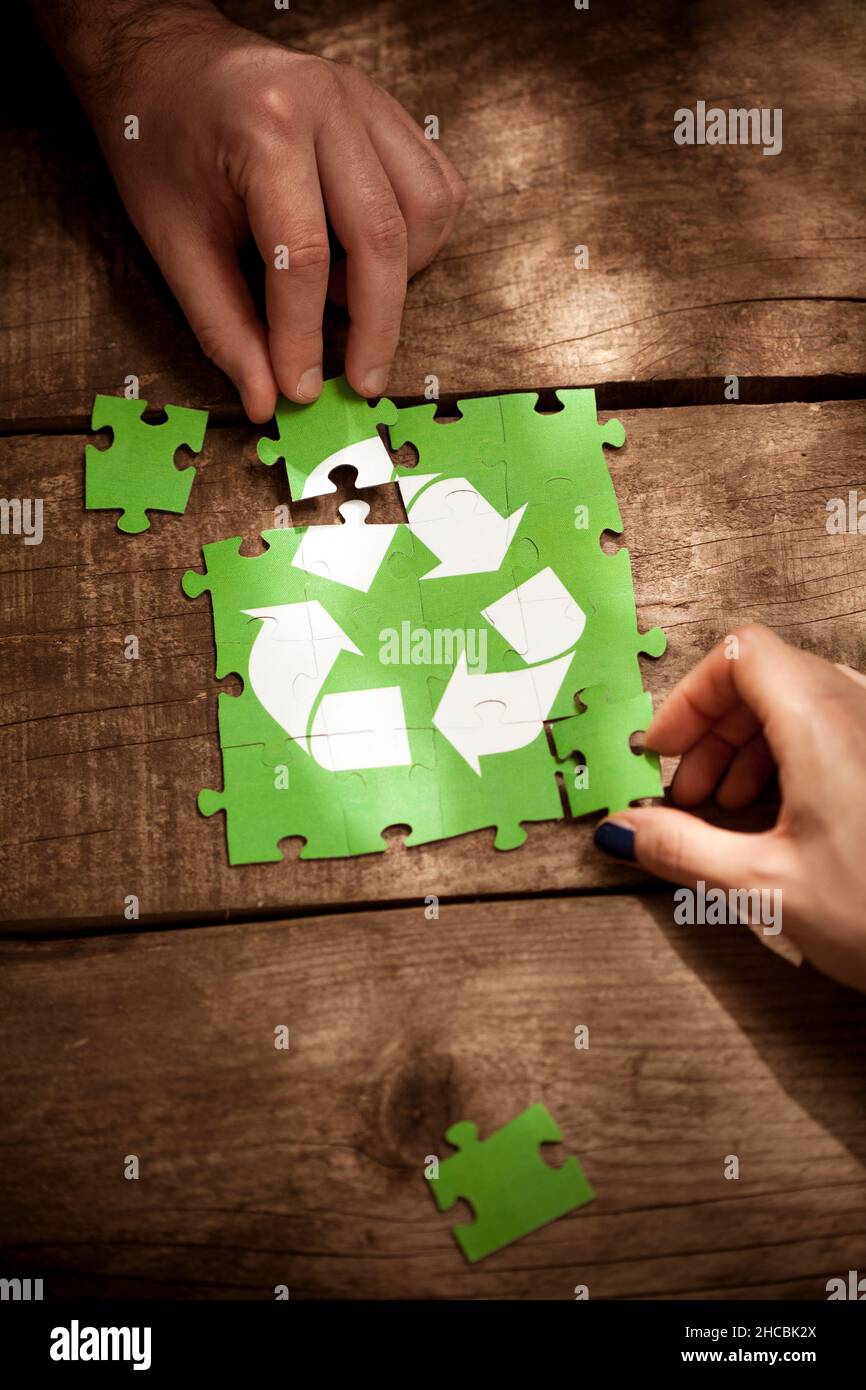 Des amis se joignent au puzzle de symbole de recyclage sur la table Banque D'Images
