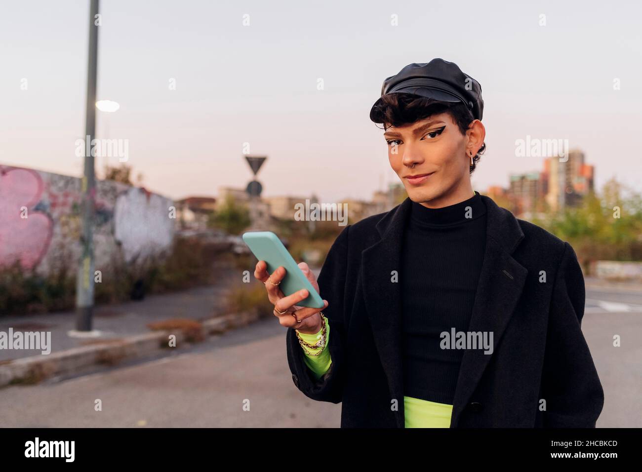 Homme gay souriant tenant le téléphone mobile sur la route Banque D'Images