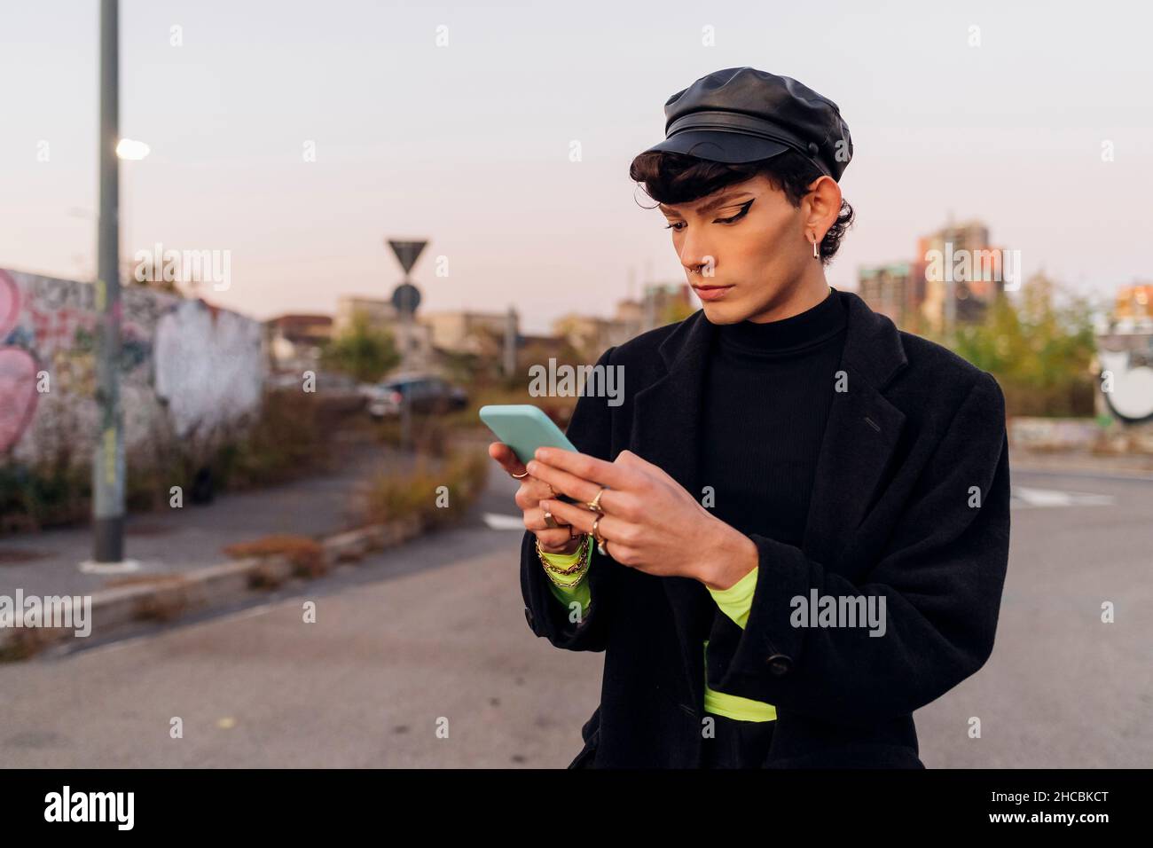 Homme gay avec Cap utilisant le téléphone mobile sur la route Banque D'Images