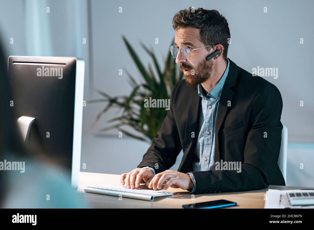 Homme d'affaires portant bluetooth travaillant sur un ordinateur au bureau Banque D'Images