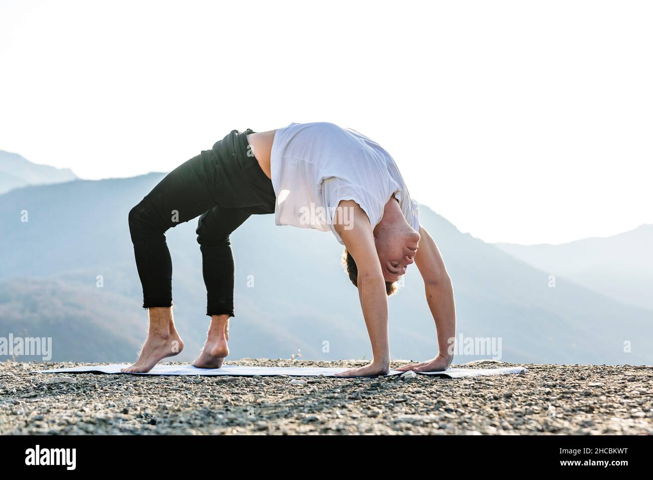 Homme pratiquant le yoga Urdhva Dhanurasana avec vue sur la montagne Banque D'Images