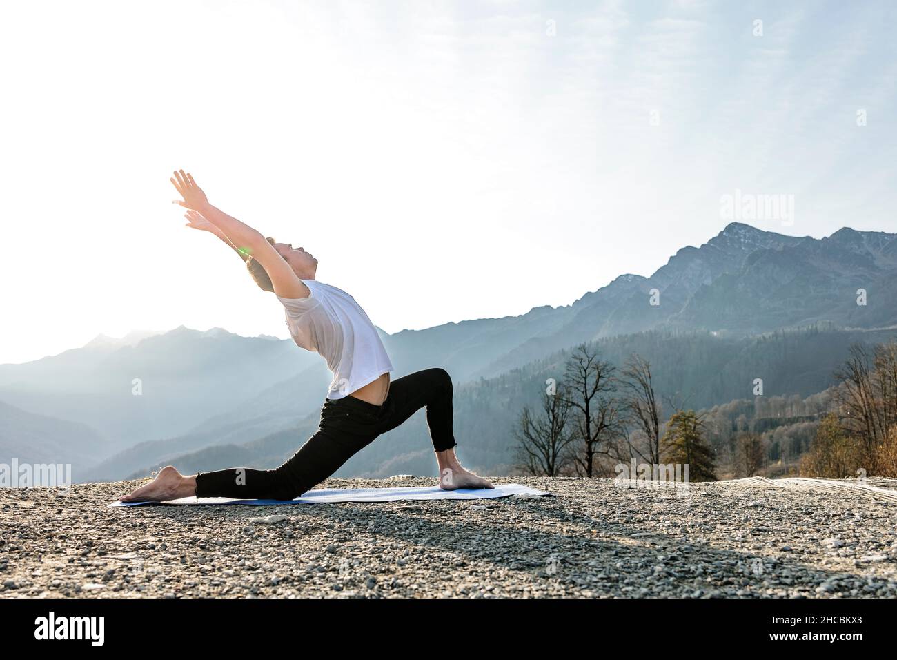 Homme avec les bras levés faisant Anjaneyasana avec vue sur la montagne Banque D'Images