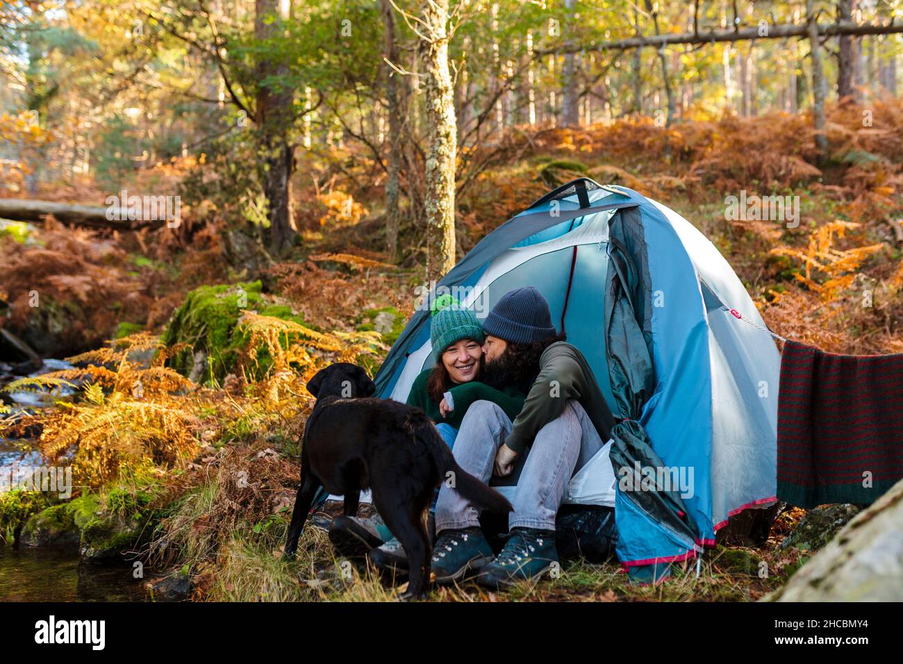 Homme embrassant petite amie par chien en tente dans la forêt d'automne Banque D'Images