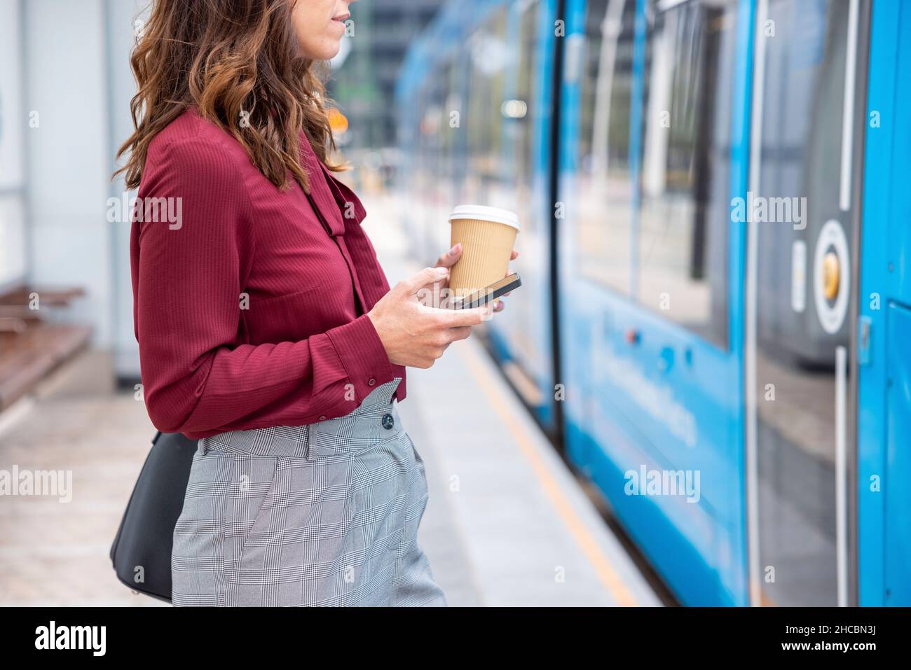 Femme d'affaires avec une tasse jetable et un smartphone s'approchant vers le train à la gare Banque D'Images