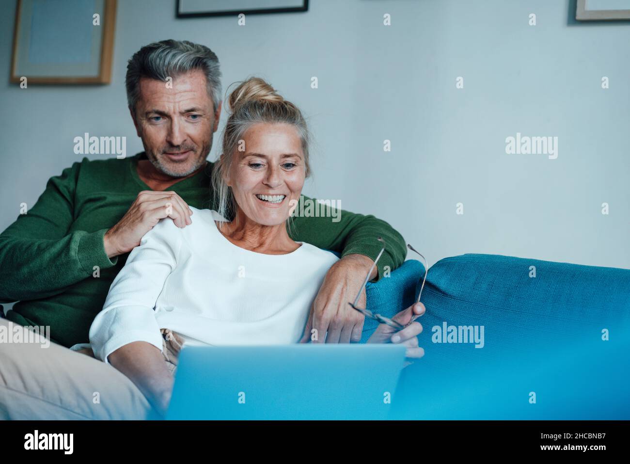 Homme assis avec le bras autour de la femme utilisant un ordinateur portable à la maison Banque D'Images