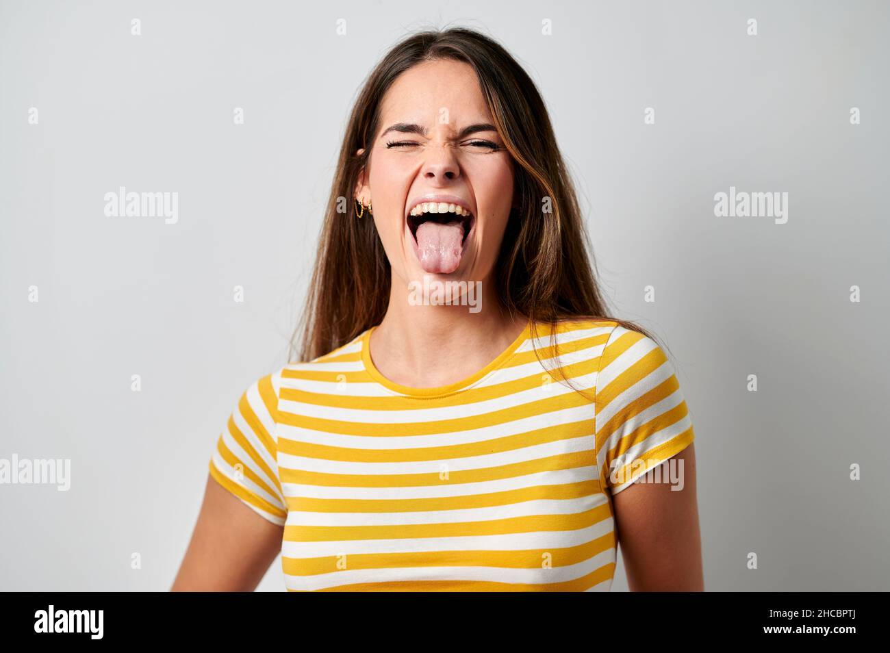 Femme gaie qui colle la langue sur fond gris Banque D'Images