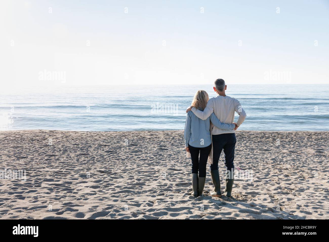 Homme avec le bras autour de la femme regardant la mer debout sur le sable Banque D'Images