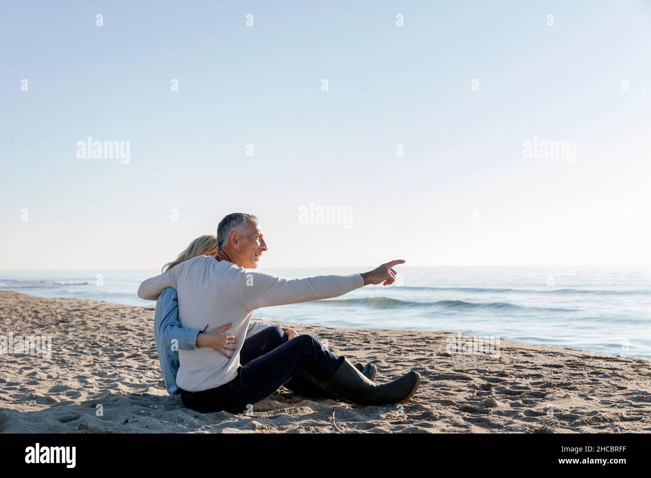 Homme pointant vers la mer assis avec le bras autour de la femme sur la plage Banque D'Images