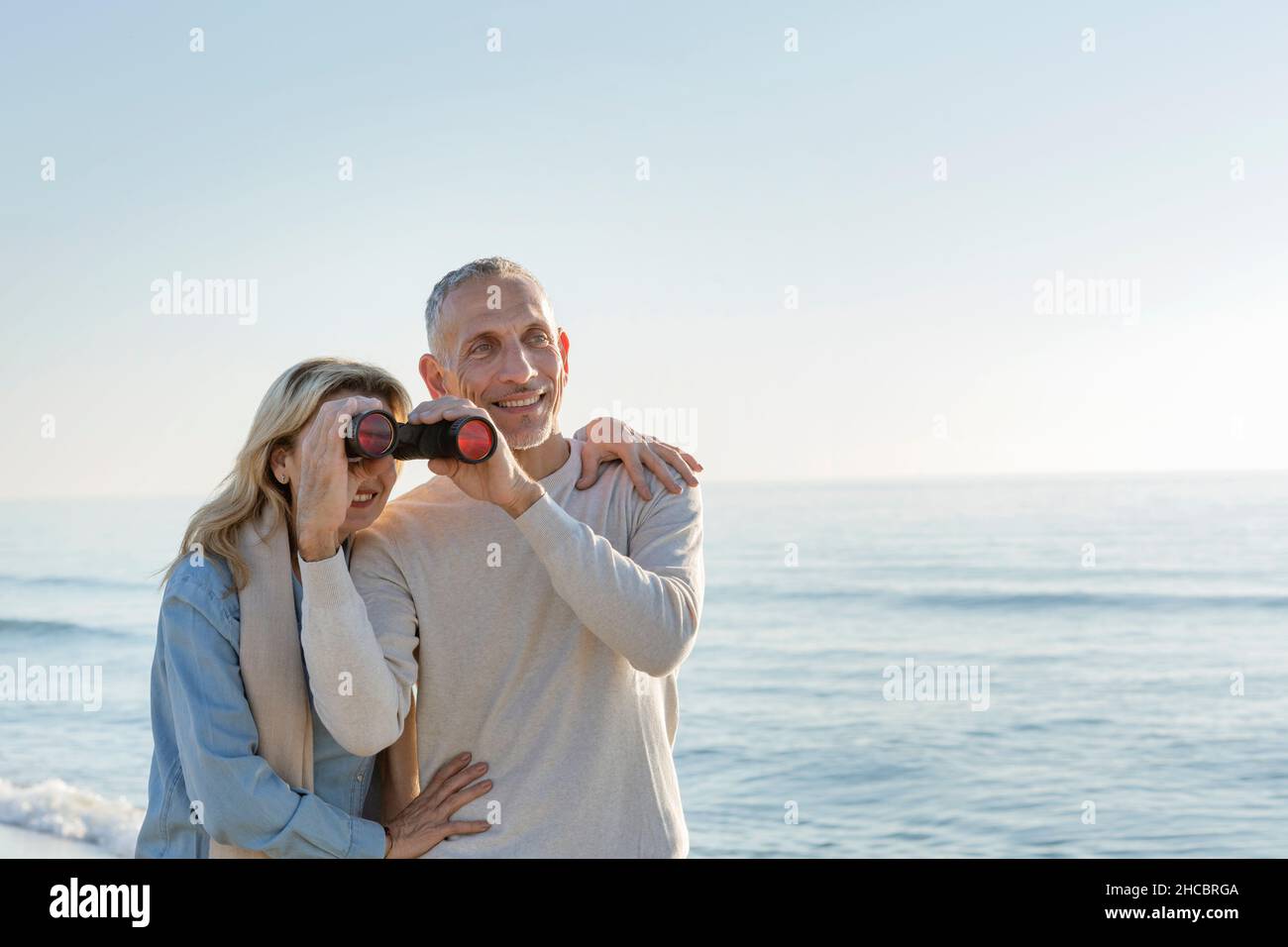 Femme regardant à travers des jumelles tenues par mari à la plage Banque D'Images