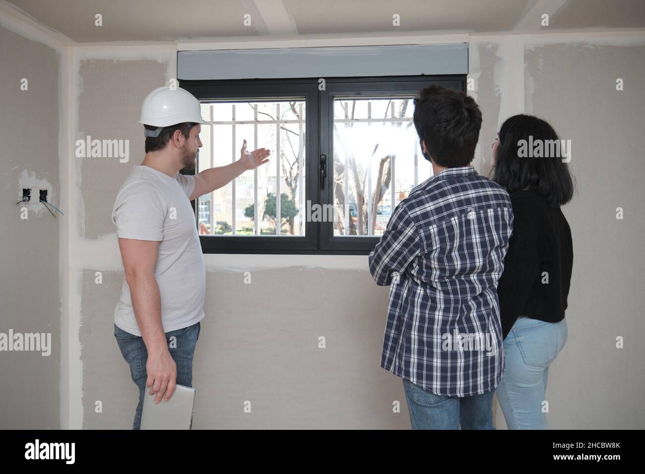 L'architecte montre la vue de la fenêtre d'un nouvel appartement à un couple. Banque D'Images