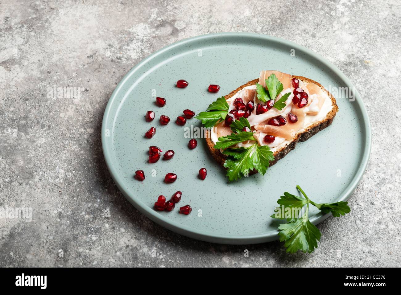 Sandwich avec jamon et herbes et grenade sur plaque bleue et fond gris vue de dessus de gros plan Banque D'Images