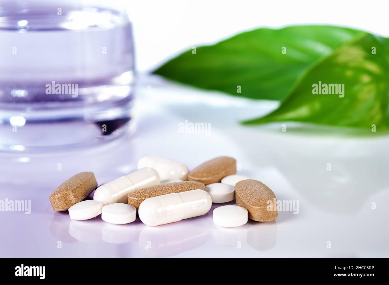 pilules blanches et caplsules, verre d'eau et feuilles vertes sur fond blanc gros plan Banque D'Images