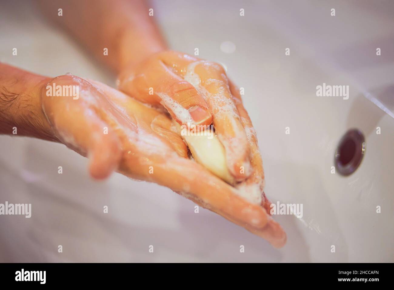 Un homme lave soigneusement ses mains avec du savon blanc sur un lavabo en céramique blanche dans la salle de bains.Propreté et hygiène. Banque D'Images