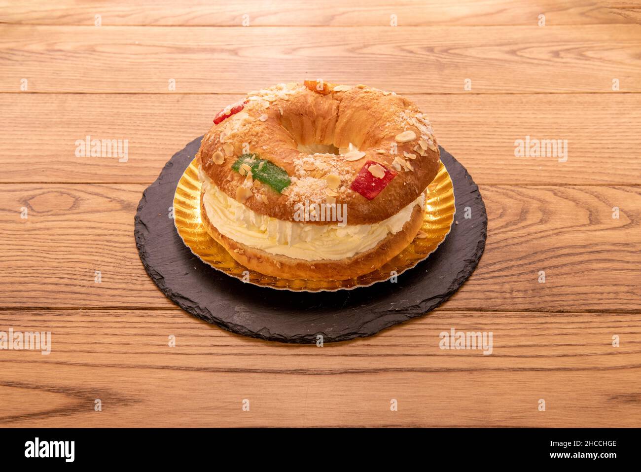 Roscón rempli de crème aux amandes, de fruits confits, de sucre glace, d'un plateau doré et d'une assiette de pizza noire Banque D'Images