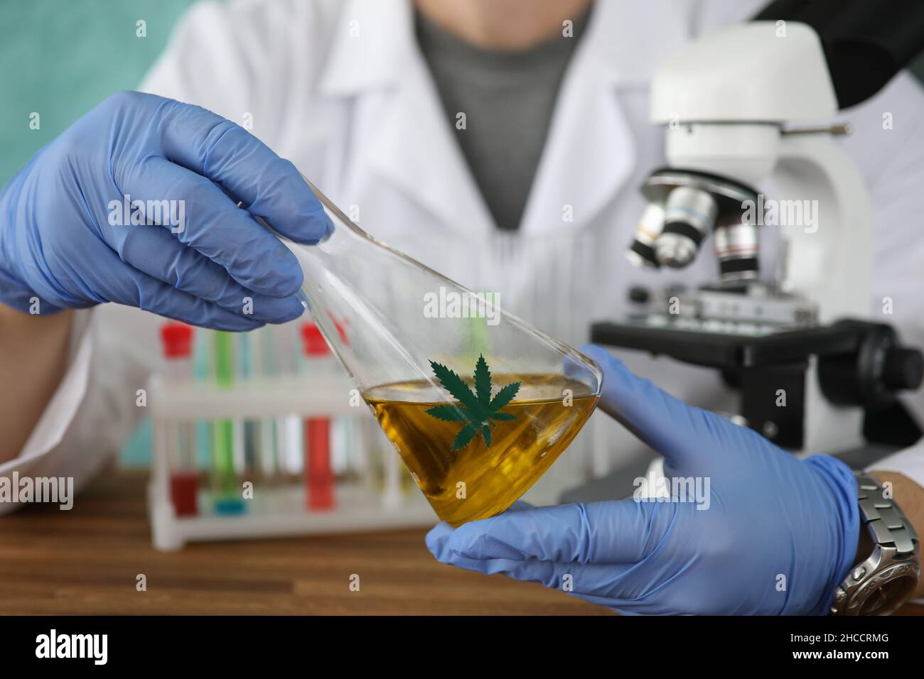 Chimiste en gants tenant une fiole avec de l'huile de marijuana dans un laboratoire fermé Banque D'Images