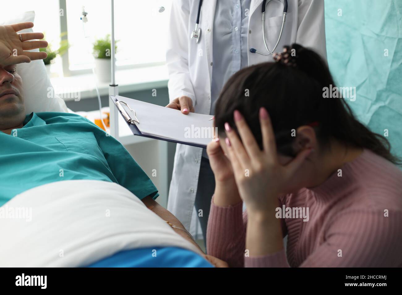 Médecin tenant des documents devant la femme et le patient qui pleurent dans la chambre d'hôpital Banque D'Images
