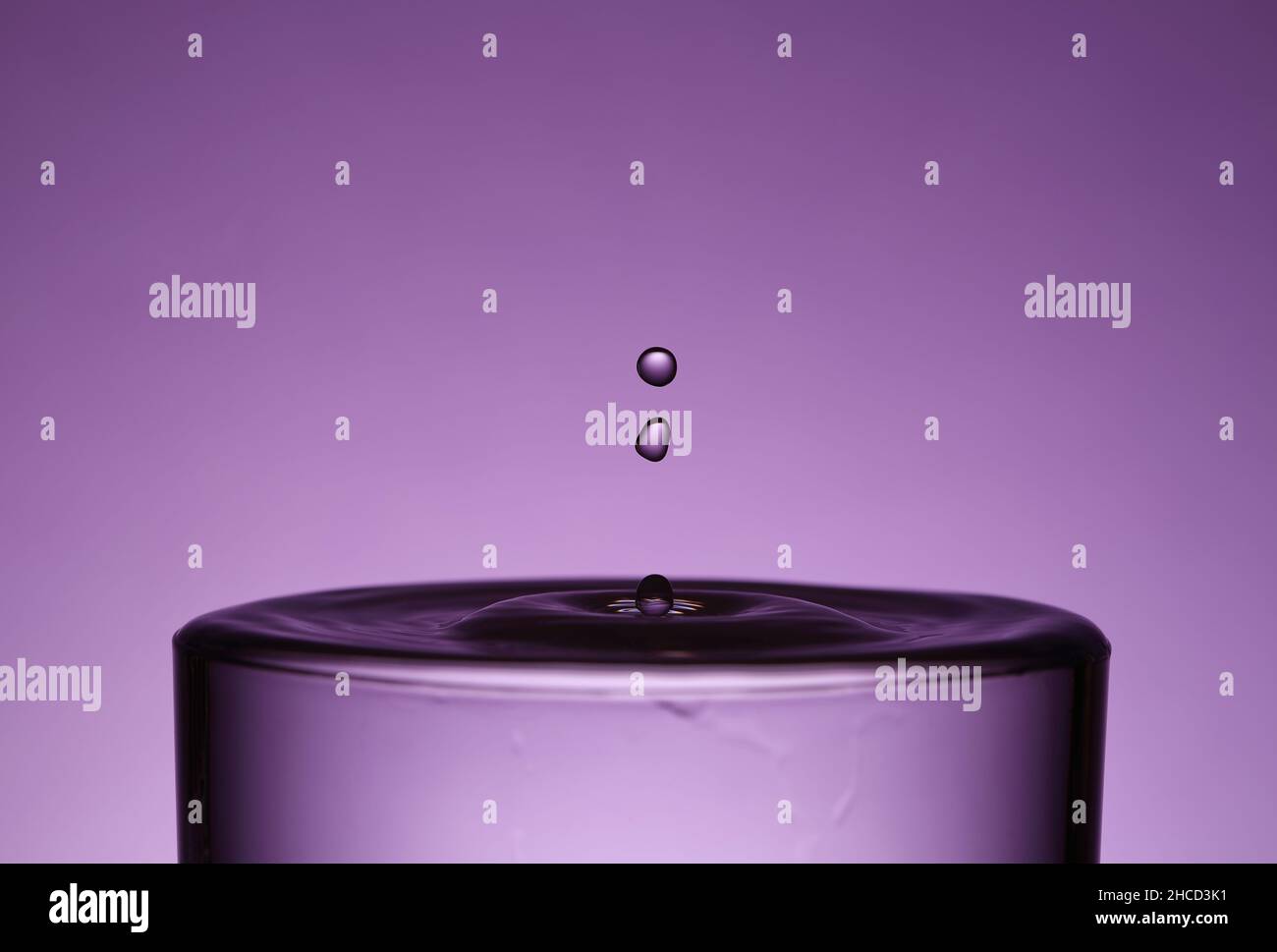 Deux gouttelettes tombent dans un verre de liquide sur fond violet Banque D'Images