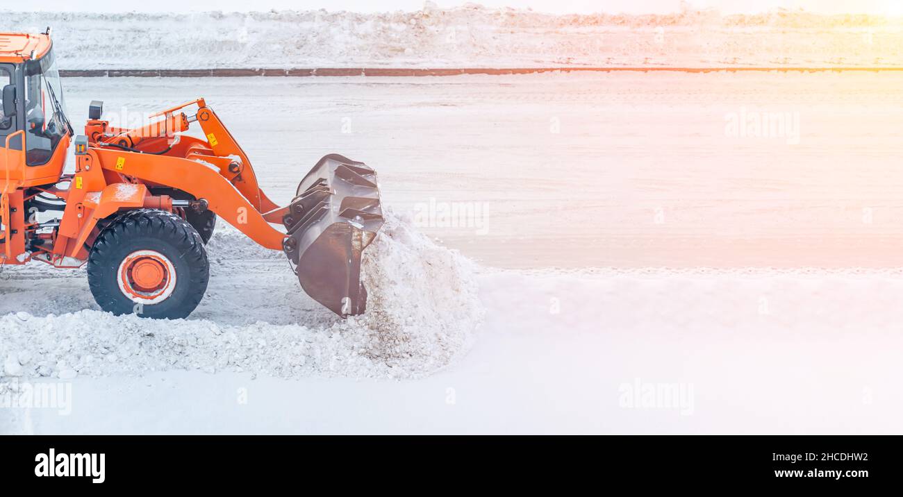 Un gros tracteur orange nettoie la neige de la route et la charge dans le camion.Nettoyage et nettoyage des routes de la ville de la neige en hiver dans le rayon Banque D'Images