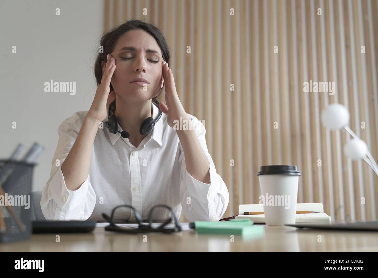 Femme italienne frustrée avec les yeux fermés massant les temples, souffrant de maux de tête au travail Banque D'Images