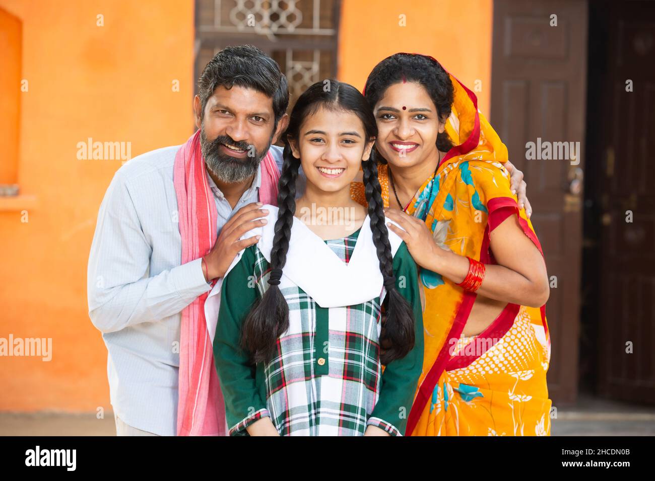 Portrait de famille indienne heureuse debout à l'extérieur de leur maison dans le village souriant parents avec leur adorable jeune fille dans la tenue traditionnelle Banque D'Images