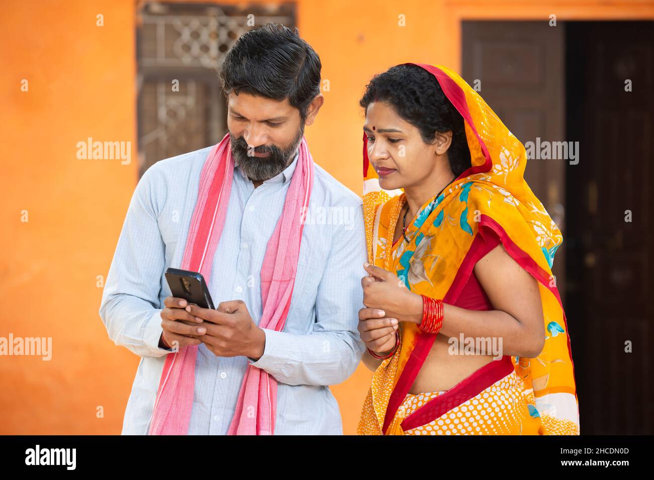Traditionnel indien rural fermier couple utilisant le smartphone pour faire le paiement en ligne , shopping sur Internet avec le téléphone portable système de service bancaire sécurisé co Banque D'Images