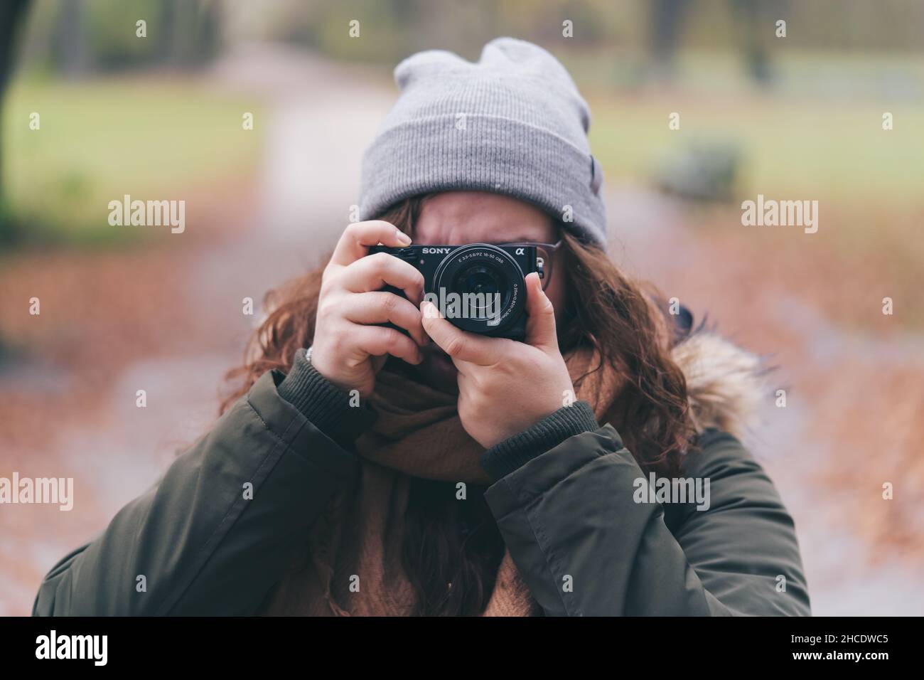Dame portant un manteau d'hiver, un chapeau et un foulard portant un Sony A6000 pour prendre des photos dans un parc Banque D'Images