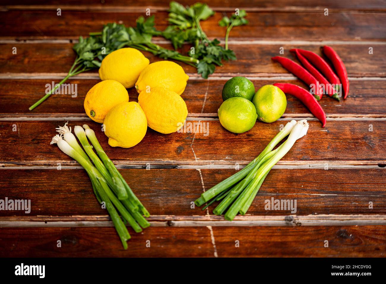 Les ingrédients frais, le citron, le citron vert, les échalotes, les piments et les herbes sont disposés avec art sur une table en bois Banque D'Images