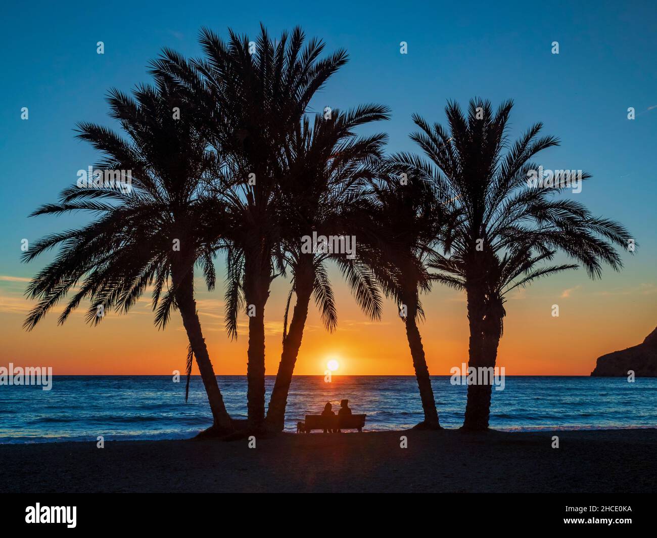 Silhouette d'un couple avec un chien sur la rive sablonneuse de la plage d'Almuñecar au coucher du soleil. Banque D'Images