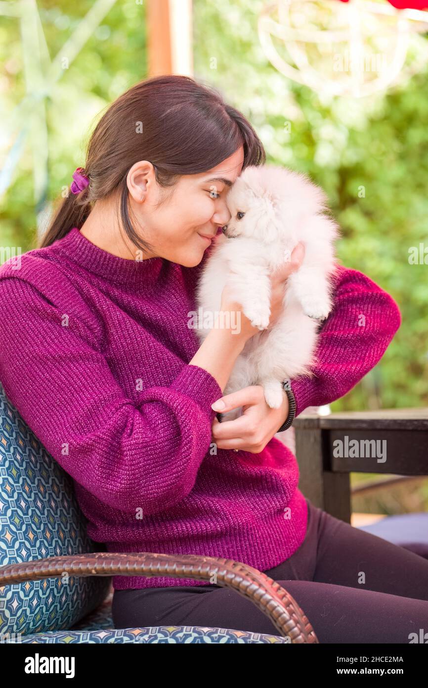 Jeune femme biracial en chandail violet tenant un petit chiot pomeranien blanc dehors sur le pont Banque D'Images