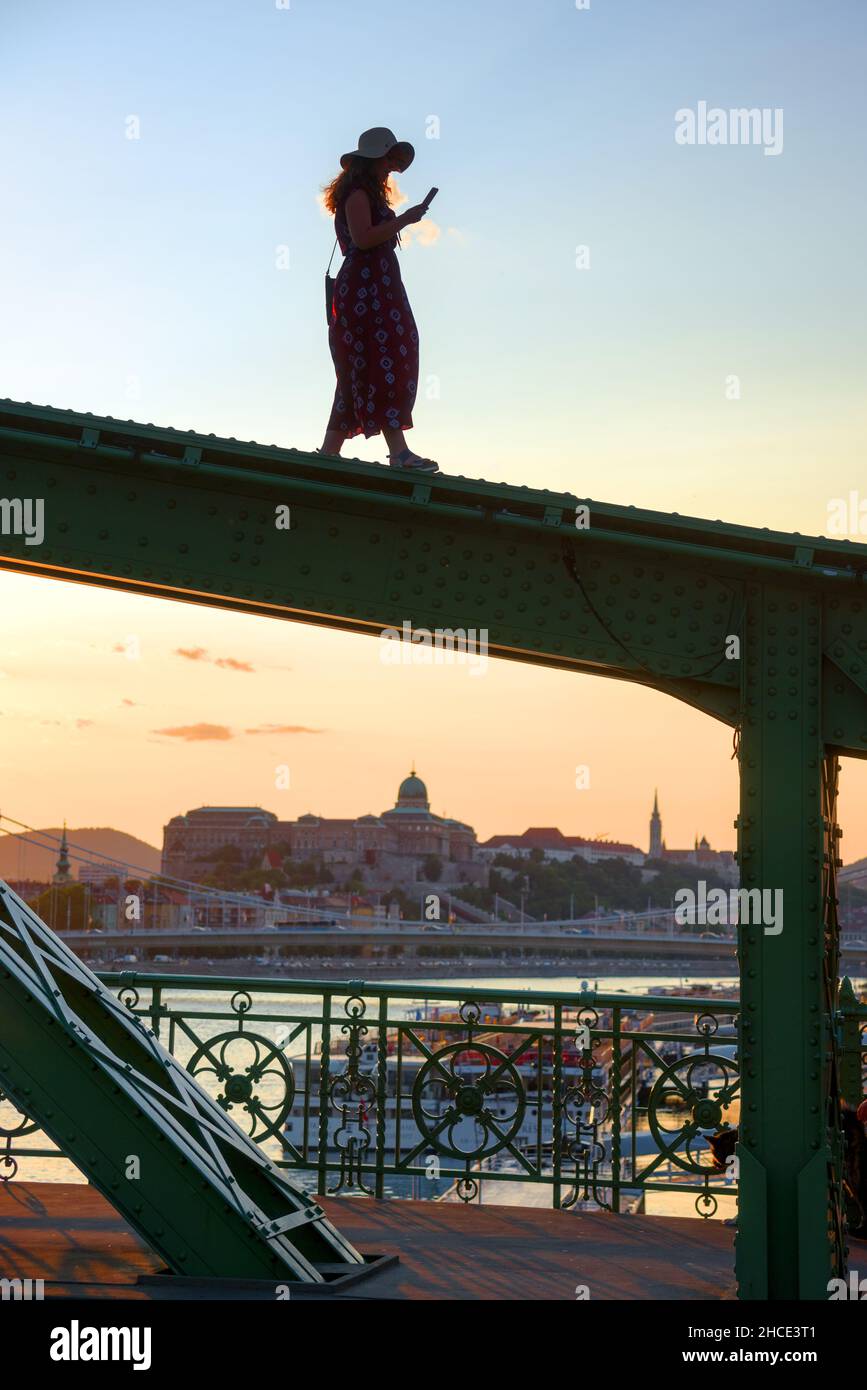 Jeune femme marchant sur le faisceau du pont en regardant son téléphone contre la vue de la ville Banque D'Images