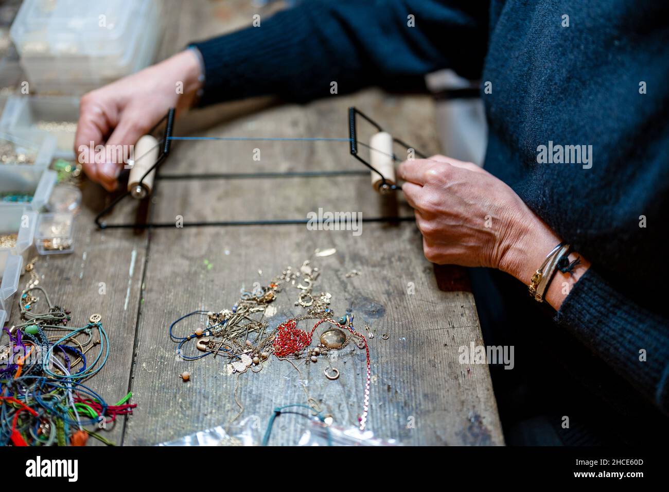 Rognez la personne anonyme en utilisant un instrument professionnel avec cordon en cuir tout en faisant de la bijouterie à la table avec divers éléments décoratifs dans l'atelier Banque D'Images