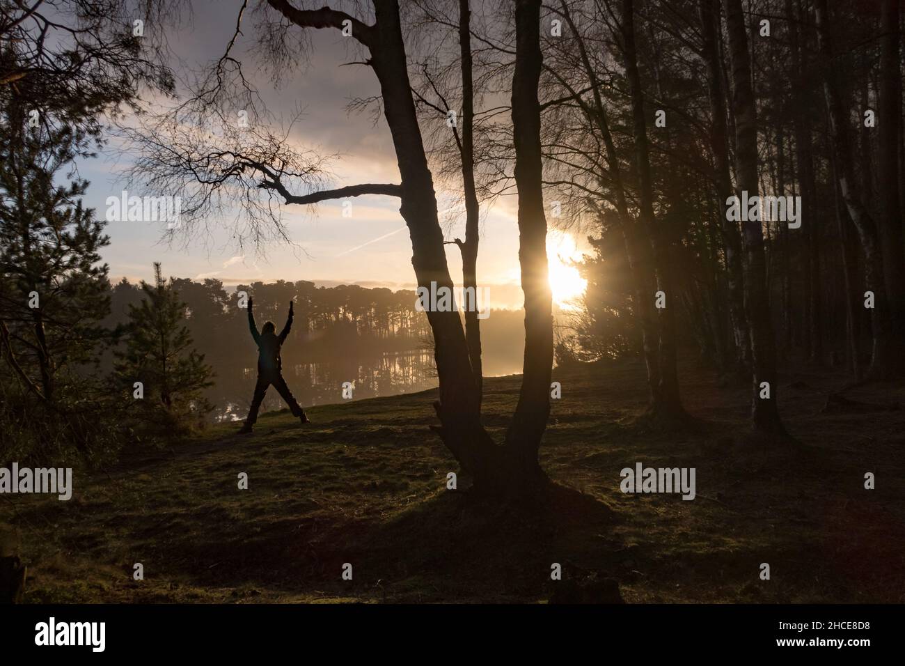 Une personne faisant des exercices au coucher du soleil dans une forêt sur la rivière d'un lac en hiver Banque D'Images