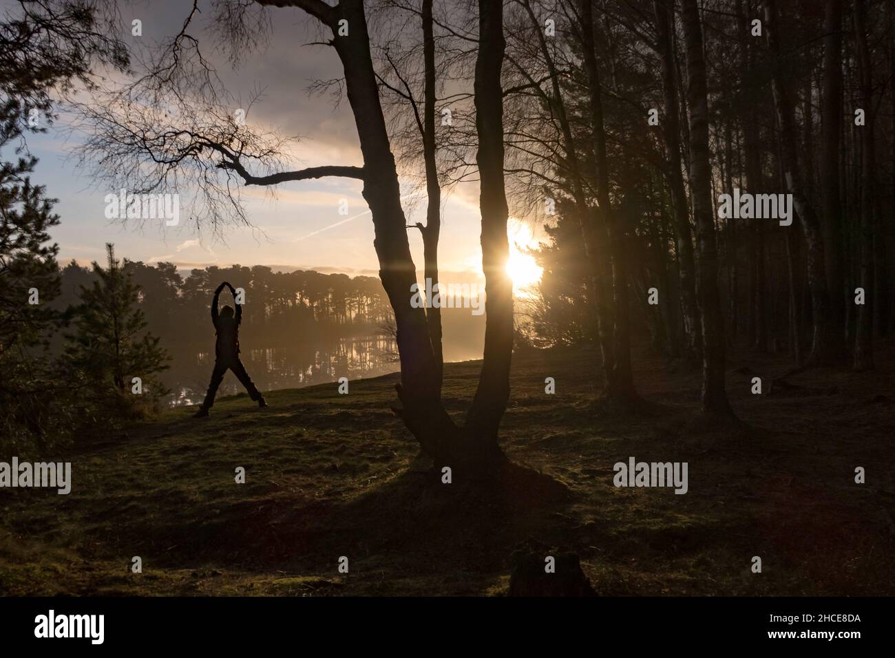 Une personne faisant des exercices au coucher du soleil dans une forêt sur la rivière d'un lac en hiver Banque D'Images