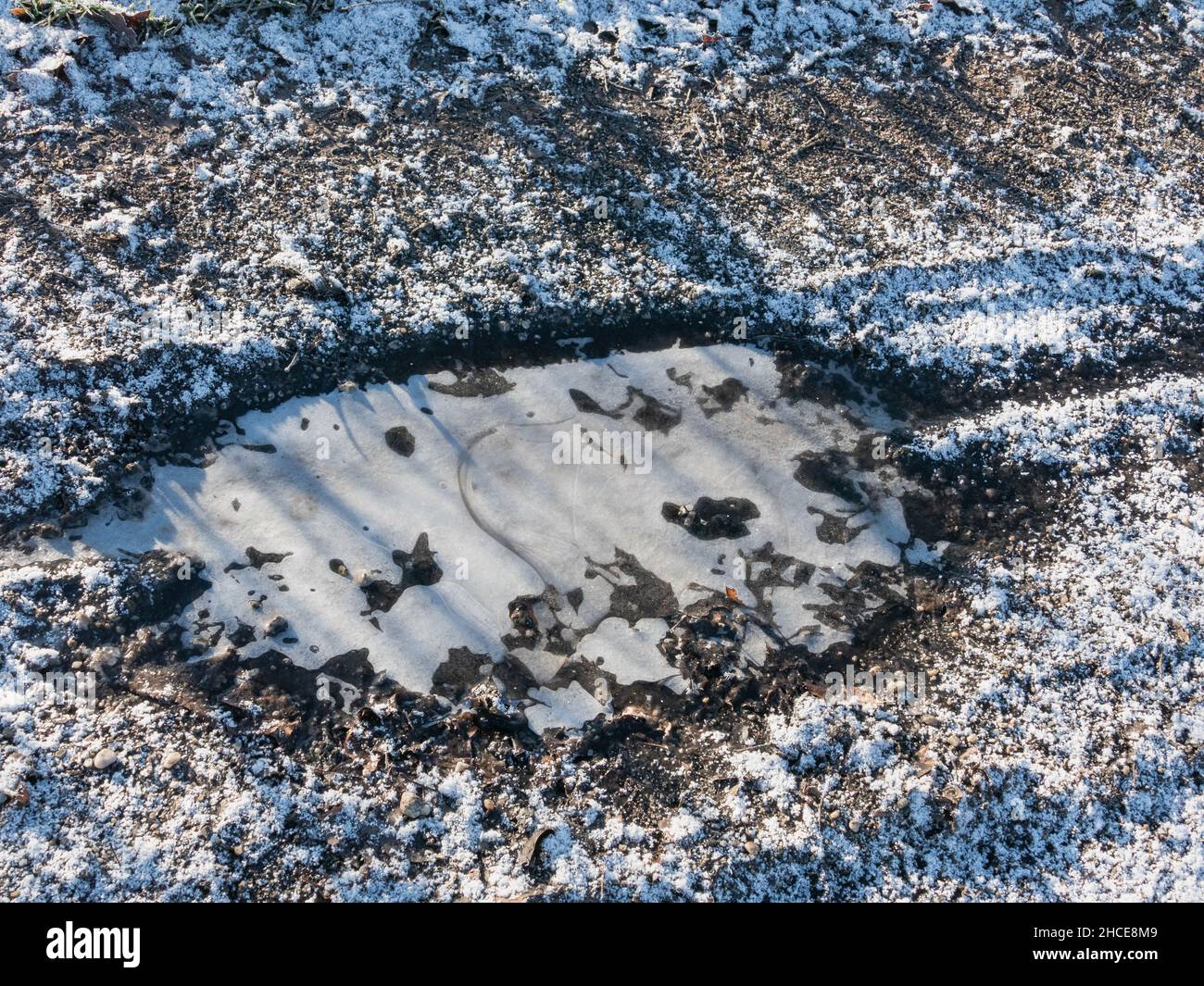 Terre, route non pavée.C'est un matin d'hiver.Le sol est recouvert d'une couche de neige, l'eau de la flaque est gelée. Banque D'Images